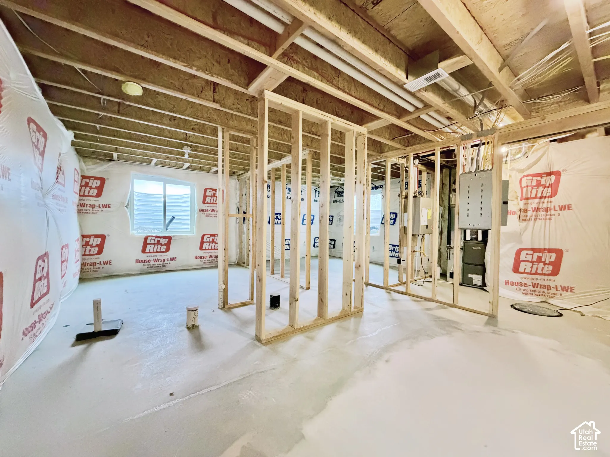 Unfinished interior space featuring exposed wood framing, concrete flooring, exterior-grade house wrap, and an installed electrical panel