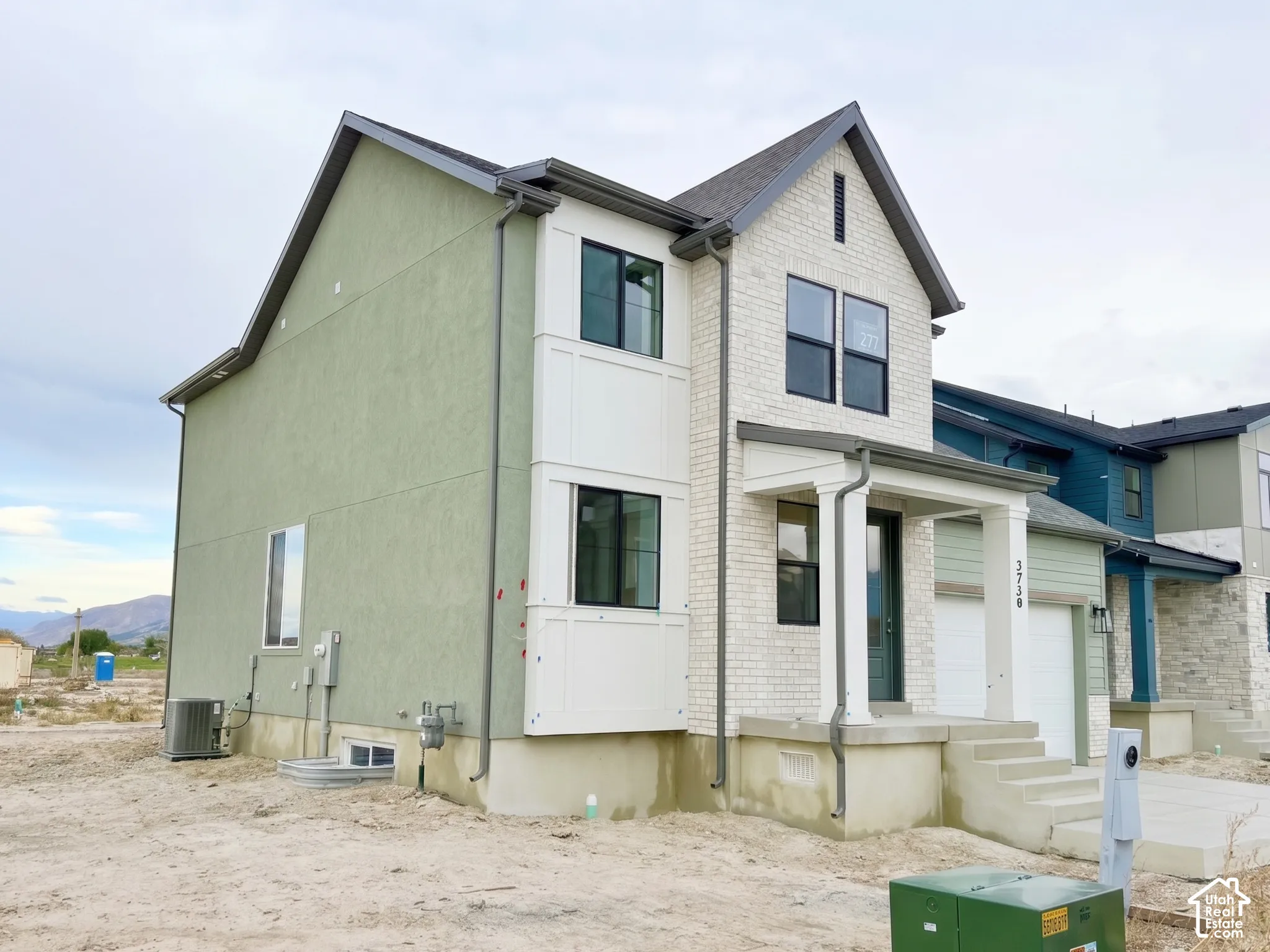 Multi-story exterior featuring a combination of stucco and brick siding, covered front entryway with square columns, and a double-car garage