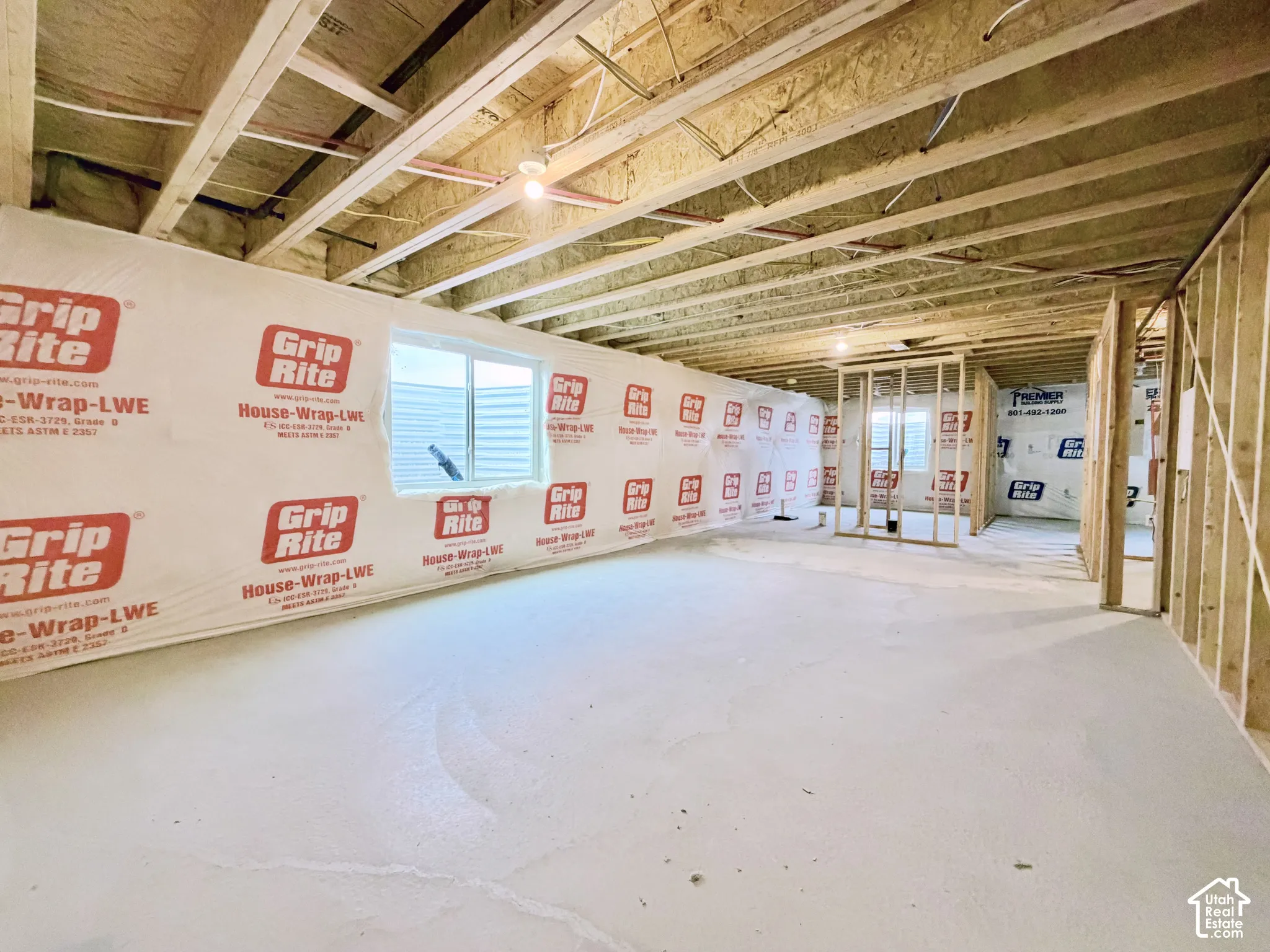 Unfinished interior space featuring exposed wood-framed joists, concrete flooring, exterior house wrap, and a sliding window