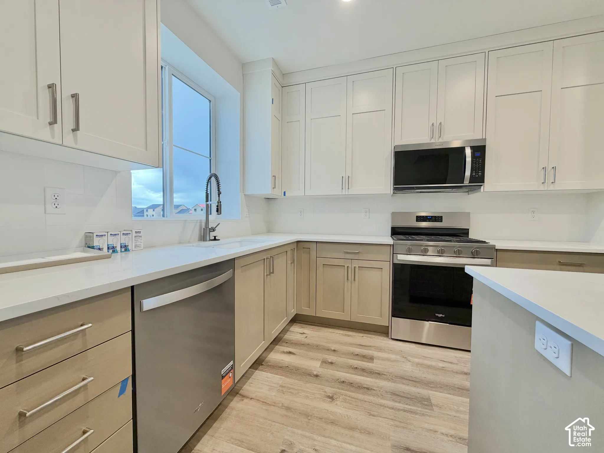 Kitchen featuring white upper cabinetry, light-toned lower cabinetry, quartz countertops, wood-finish flooring, and stainless steel appliances
