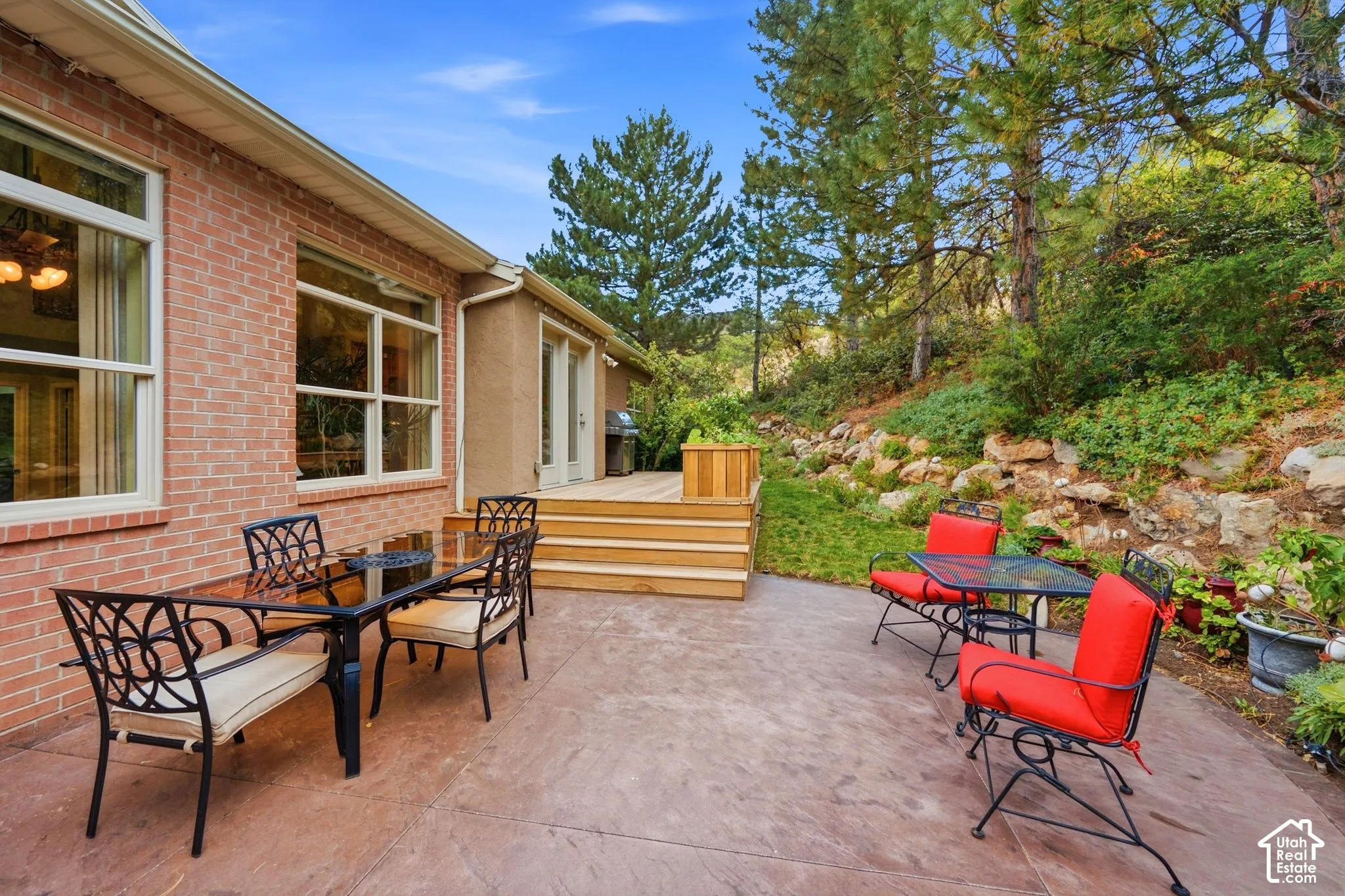 Exterior space featuring a brick facade, stamped concrete patio, tiered wood deck, and terraced natural rock retaining wall