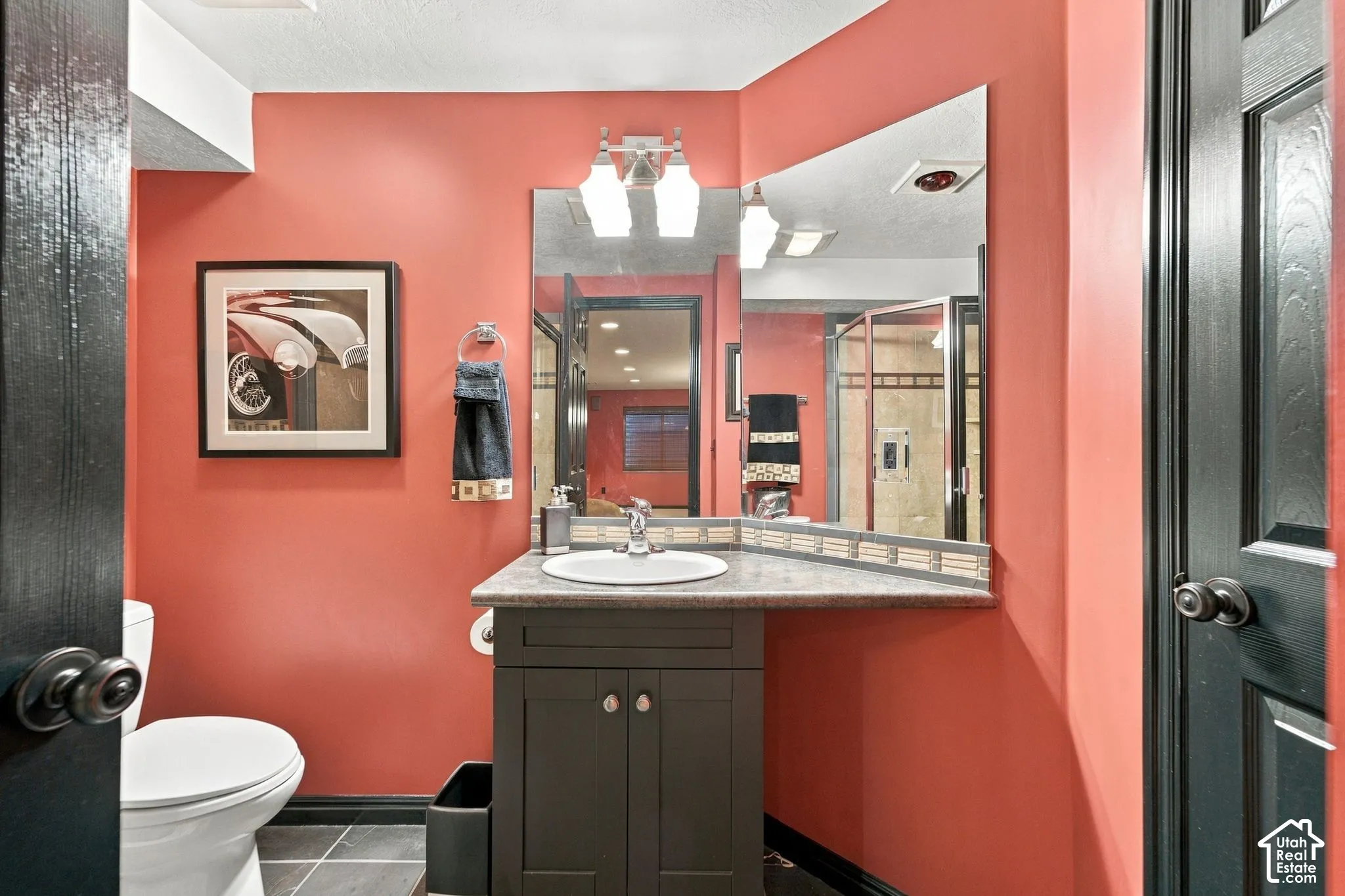 Corner vanity with dark-finish cabinetry, solid-surface countertop, and integrated sink, complemented by a tri-light fixture, large wall-mounted mirror, and tile flooring
