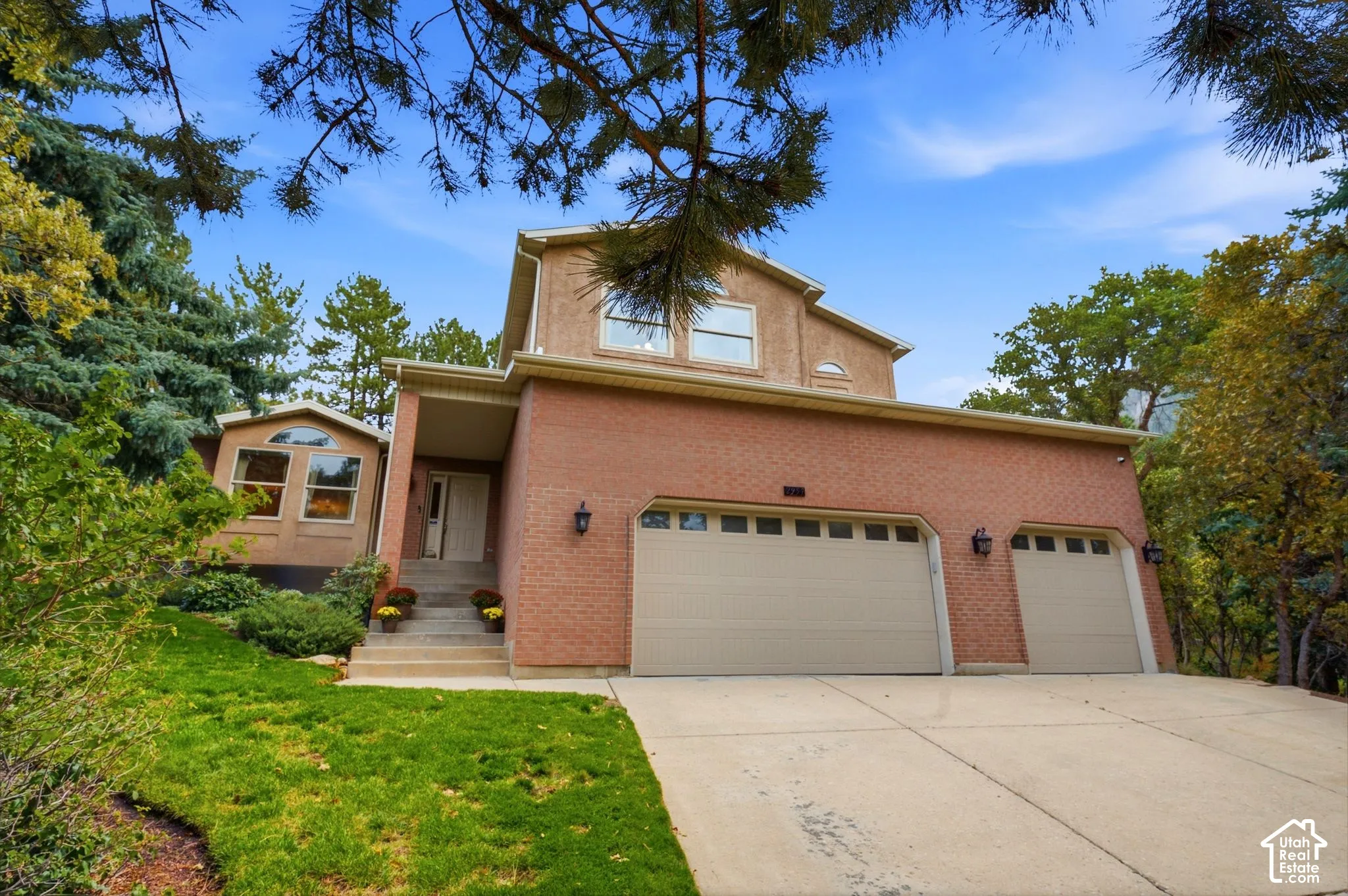 Multi-level exterior featuring a brick facade, three-car garage with overhead carriage-style doors, concrete driveway, and arched window detailing
