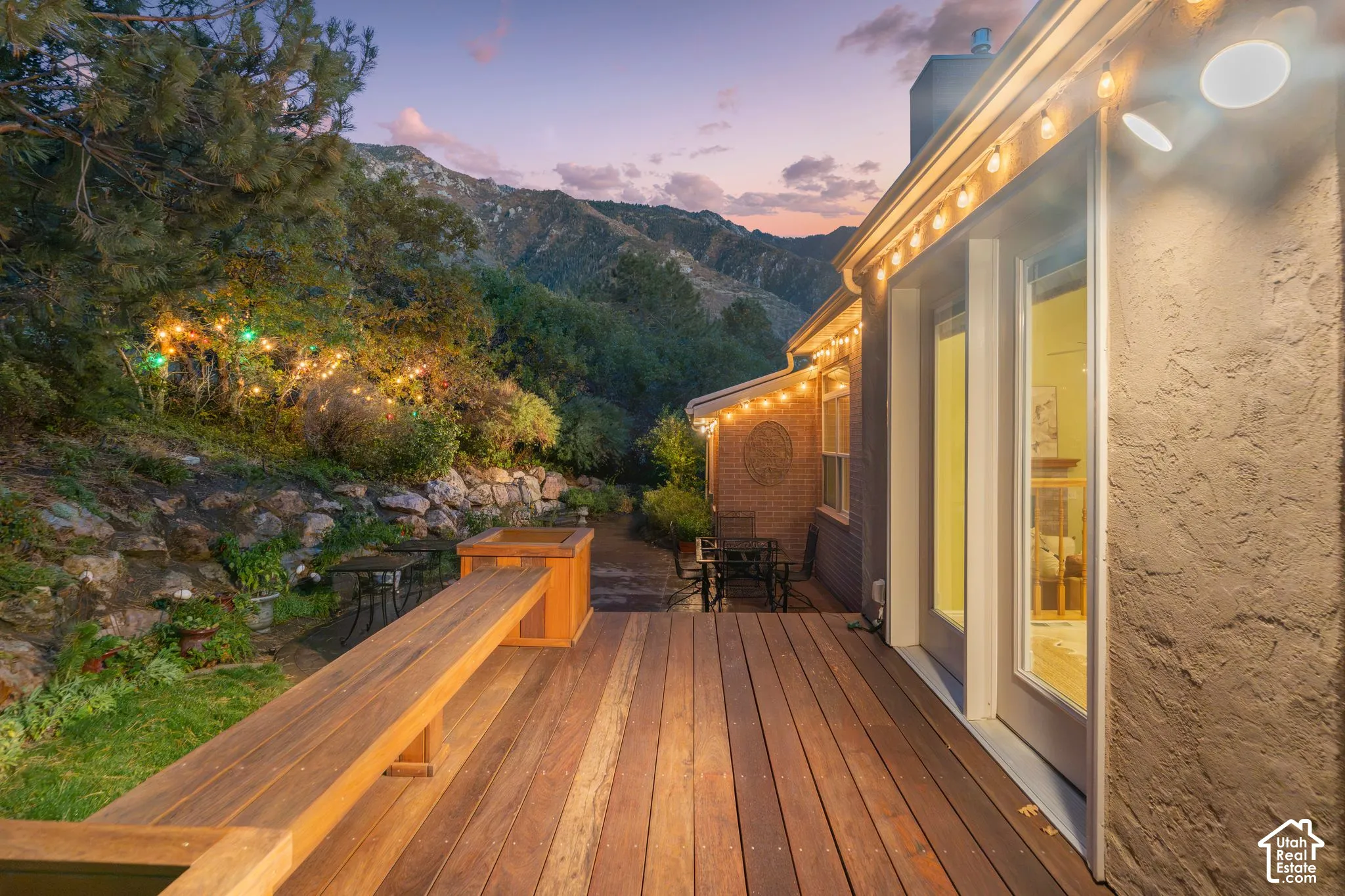 Exterior deck featuring natural wood-finish planks, integrated bench seating, stacked stone retaining wall, and mountain backdrop