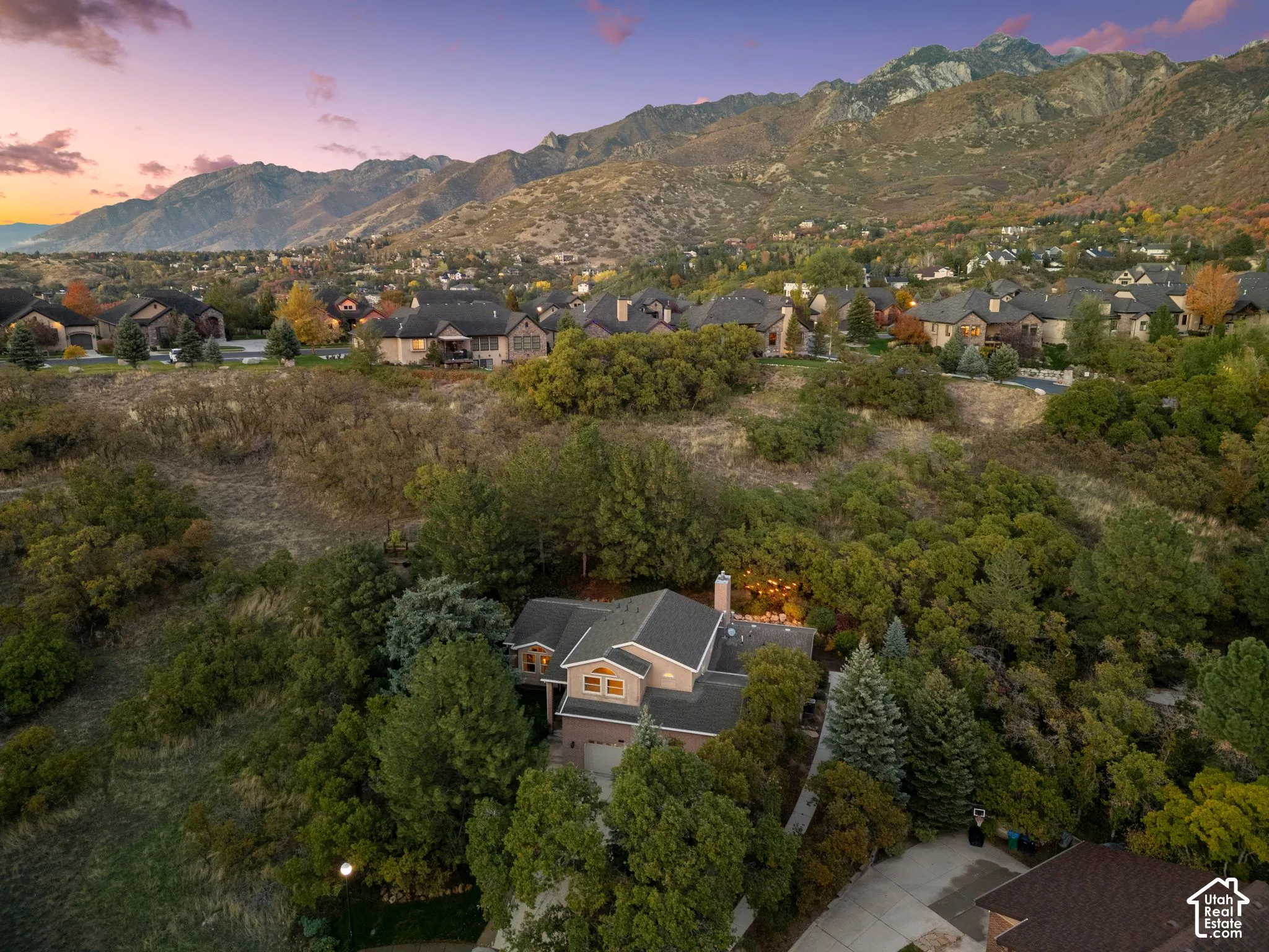 Residential property situated on a hillside lot featuring mature native trees, a pitched roofline, masonry chimney, and prominent mountain backdrop
