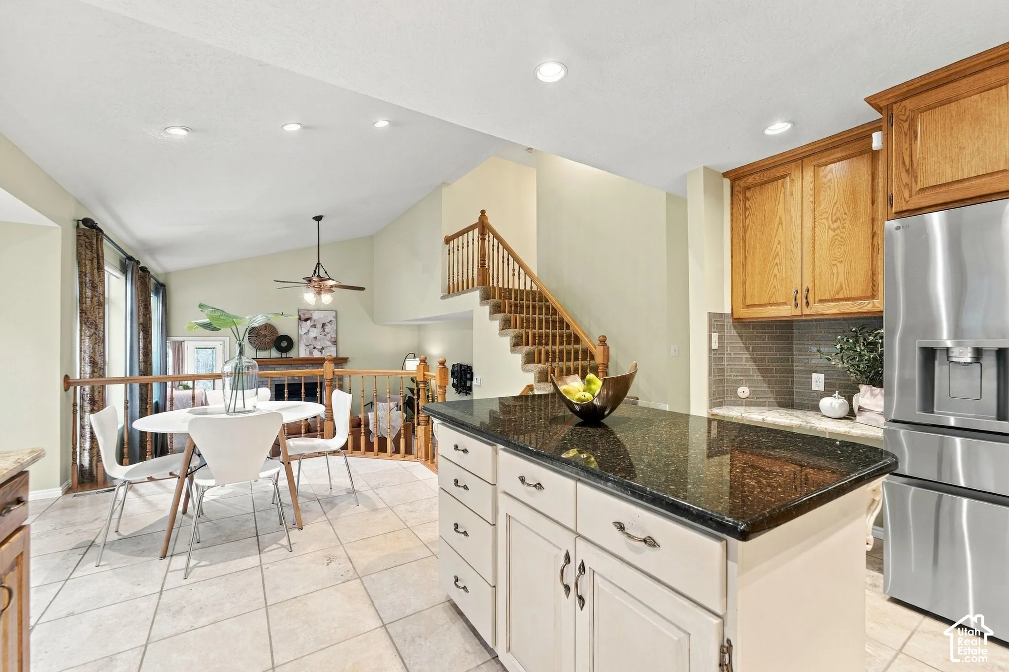 Kitchen featuring a central island with dark stone countertops, natural wood cabinetry, tile flooring, recessed lighting, and a staircase with wood railing
