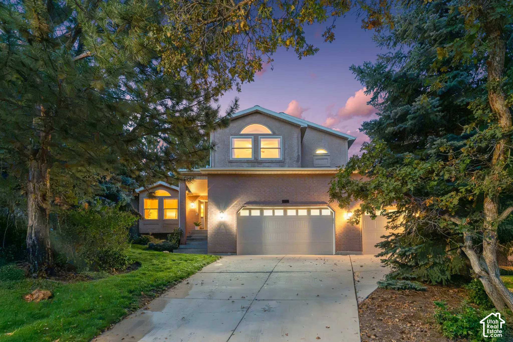 Multi-level exterior featuring a brick facade, arched accent window, attached three-car garage, concrete driveway, and mature coniferous landscaping