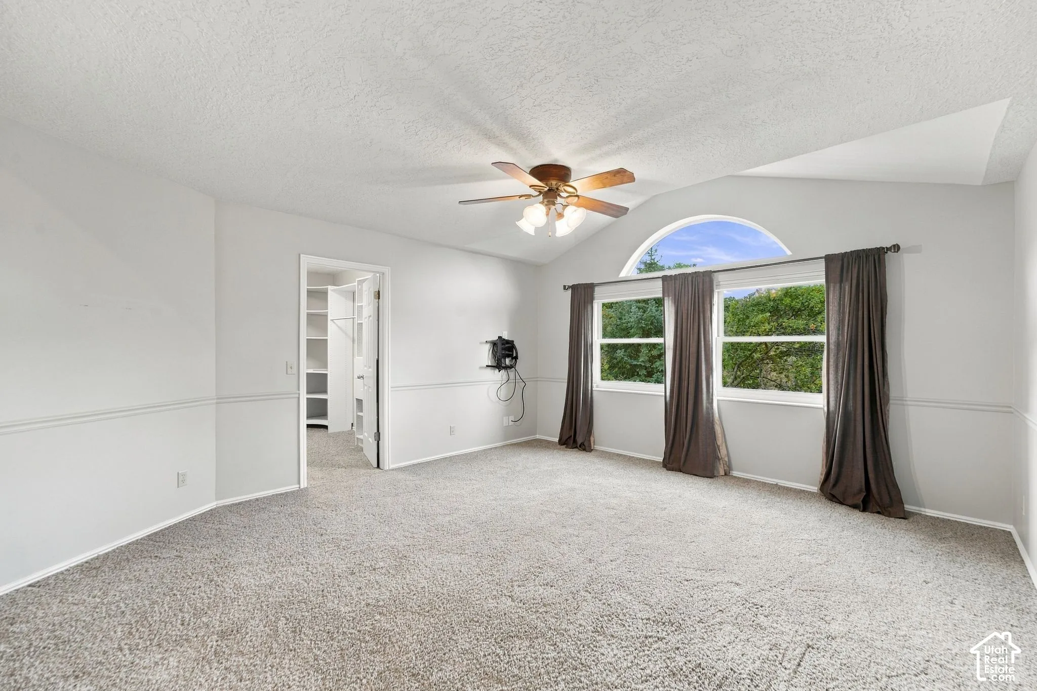 Second Floor Primary Suite with Vaulted ceiling room featuring a central arched window, wall-mounted chair rail molding, neutral carpet flooring, and a ceiling fan with integrated light fixture