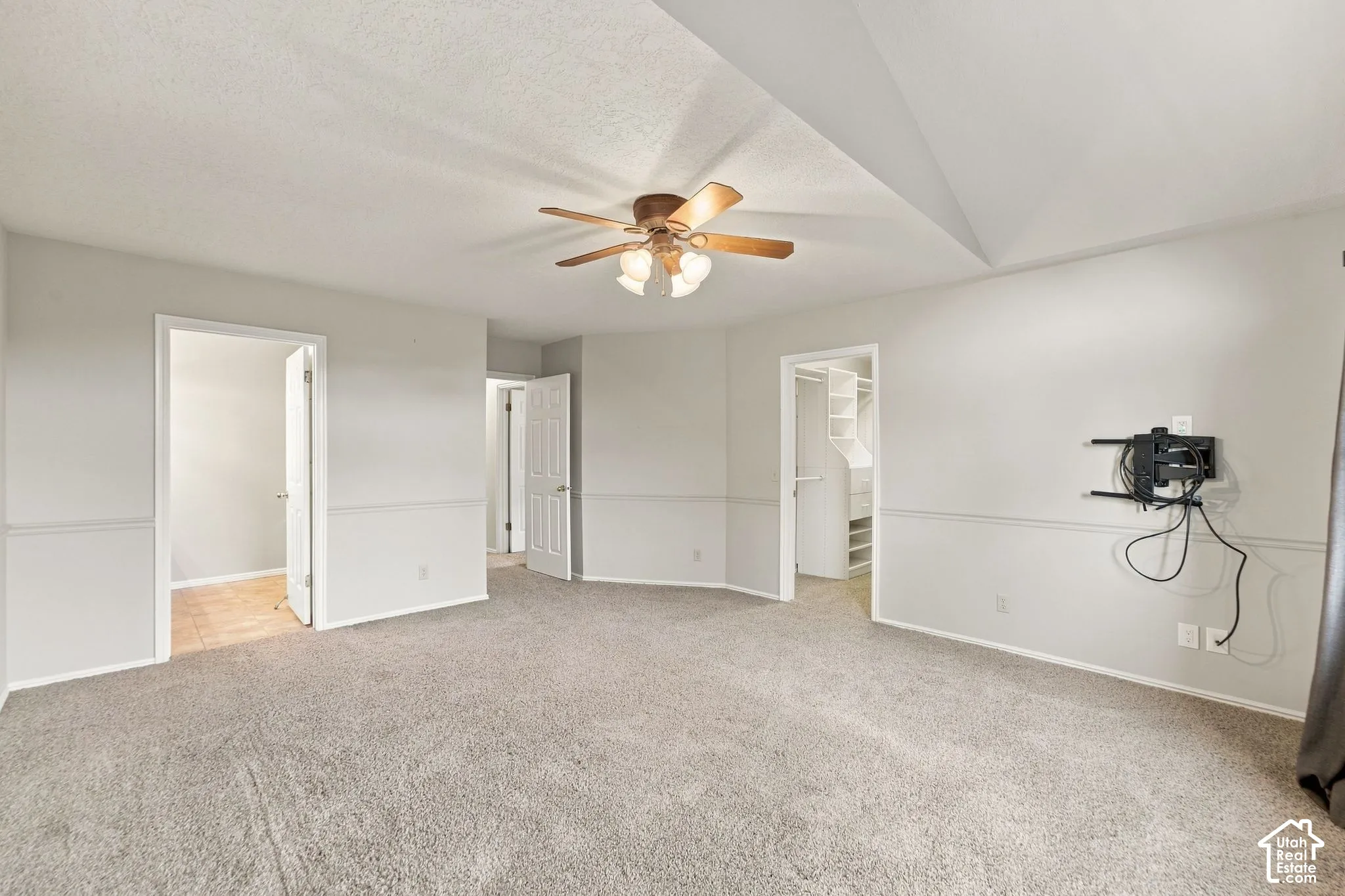 Second Floor Primary Suite with Vaulted ceiling room featuring a central arched window, wall-mounted chair rail molding, neutral carpet flooring, and a ceiling fan with integrated light fixture