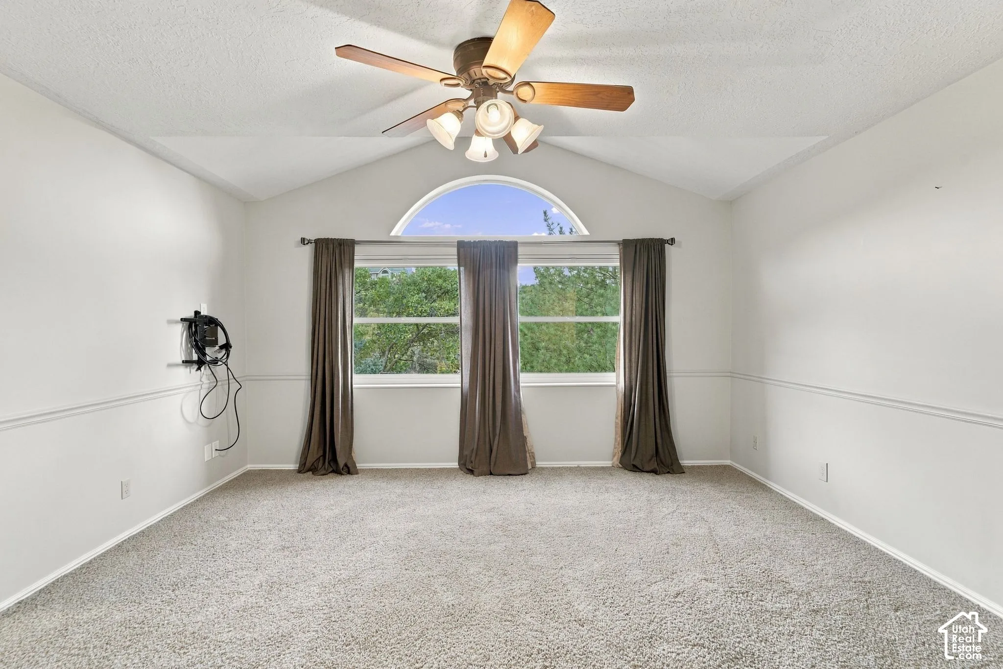 Second Floor Primary Suite with Vaulted ceiling room featuring a central arched window, wall-mounted chair rail molding, neutral carpet flooring, and a ceiling fan with integrated light fixture