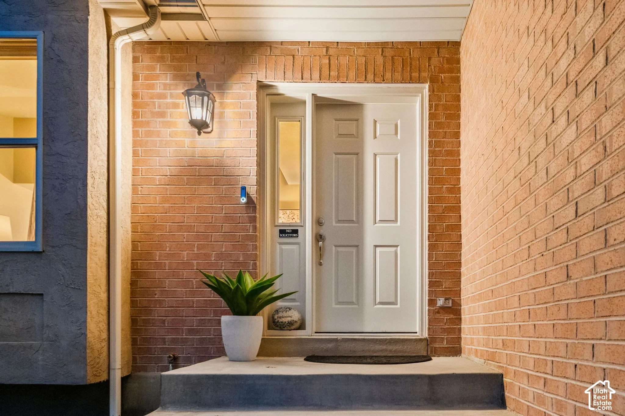 Entryway featuring a brick facade, recessed paneled door with sidelight, and an attached wall-mounted lantern fixture