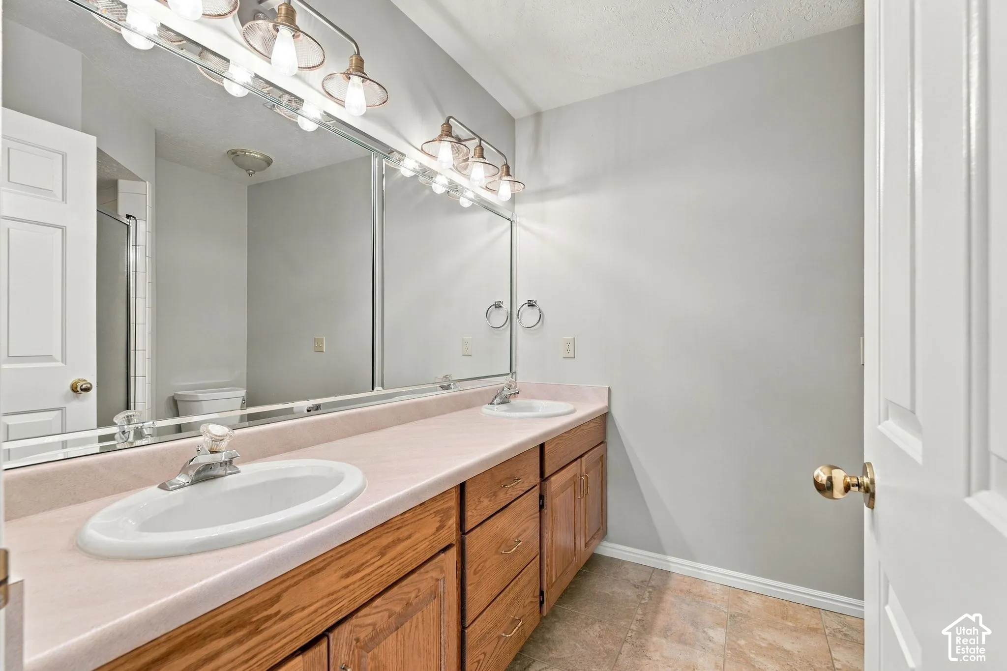 Second Floor Primary Ensuite Bathroom with Dual-sink vanity featuring a light-toned countertop, wood-finish cabinetry, a large wall-mounted mirror, and industrial-style multi-bulb lighting fixtures