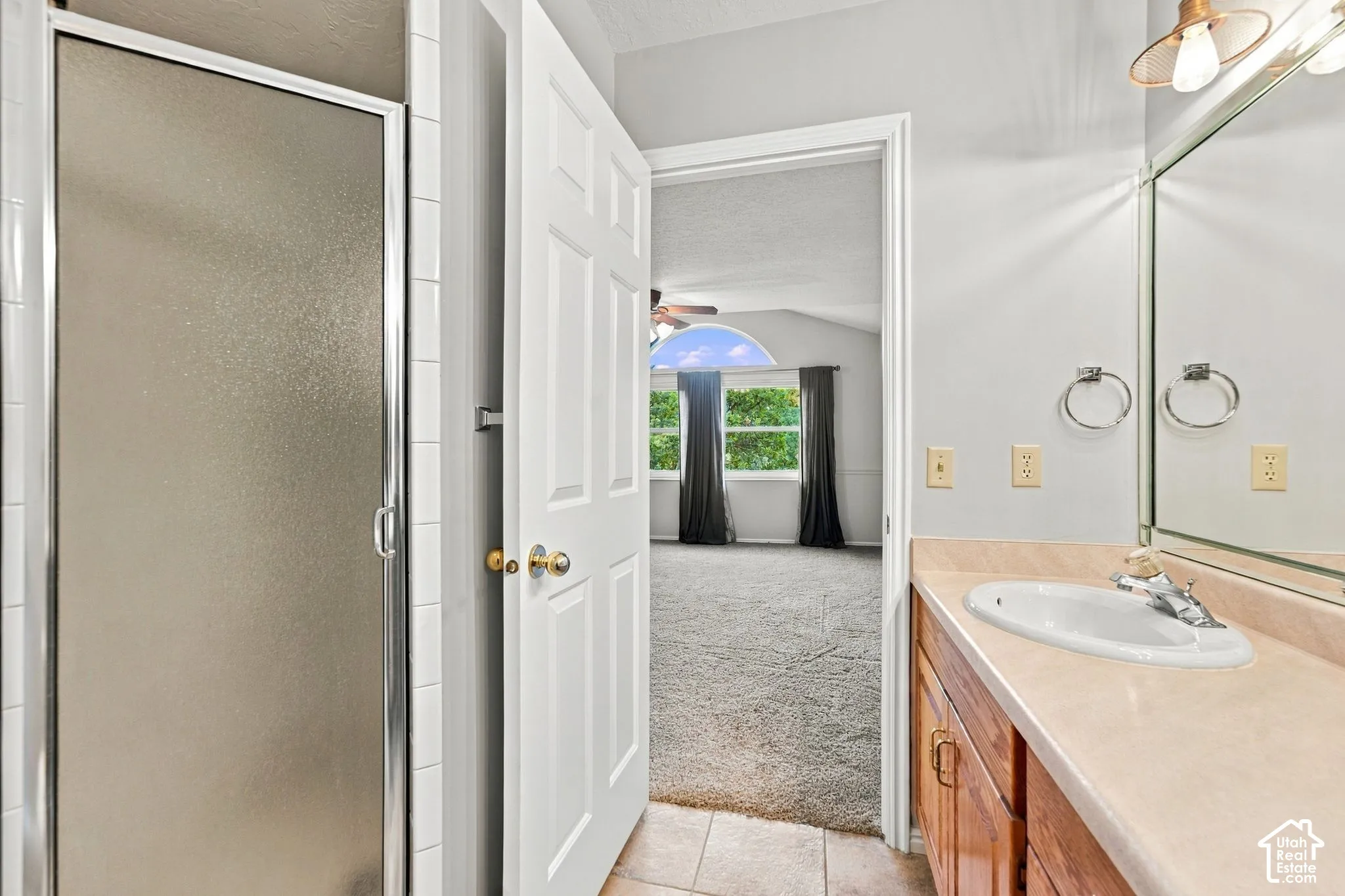 Second Floor Primary Ensuite Bathroom with Dual-sink vanity featuring a light-toned countertop, wood-finish cabinetry, a large wall-mounted mirror, and industrial-style multi-bulb lighting fixtures