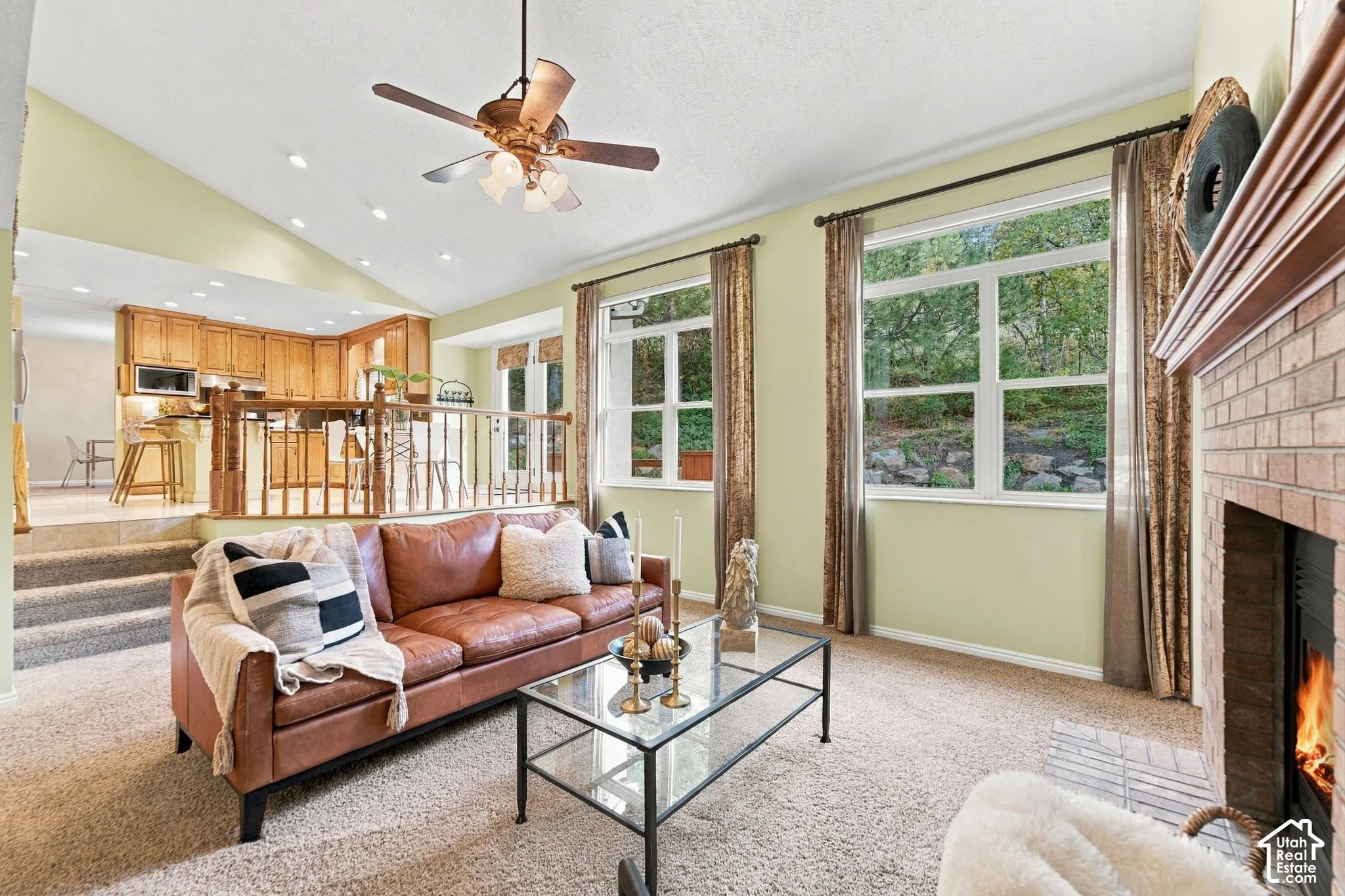 Vaulted ceilings, brick-surround fireplace, ceiling fan, and large windows with outdoor scenery