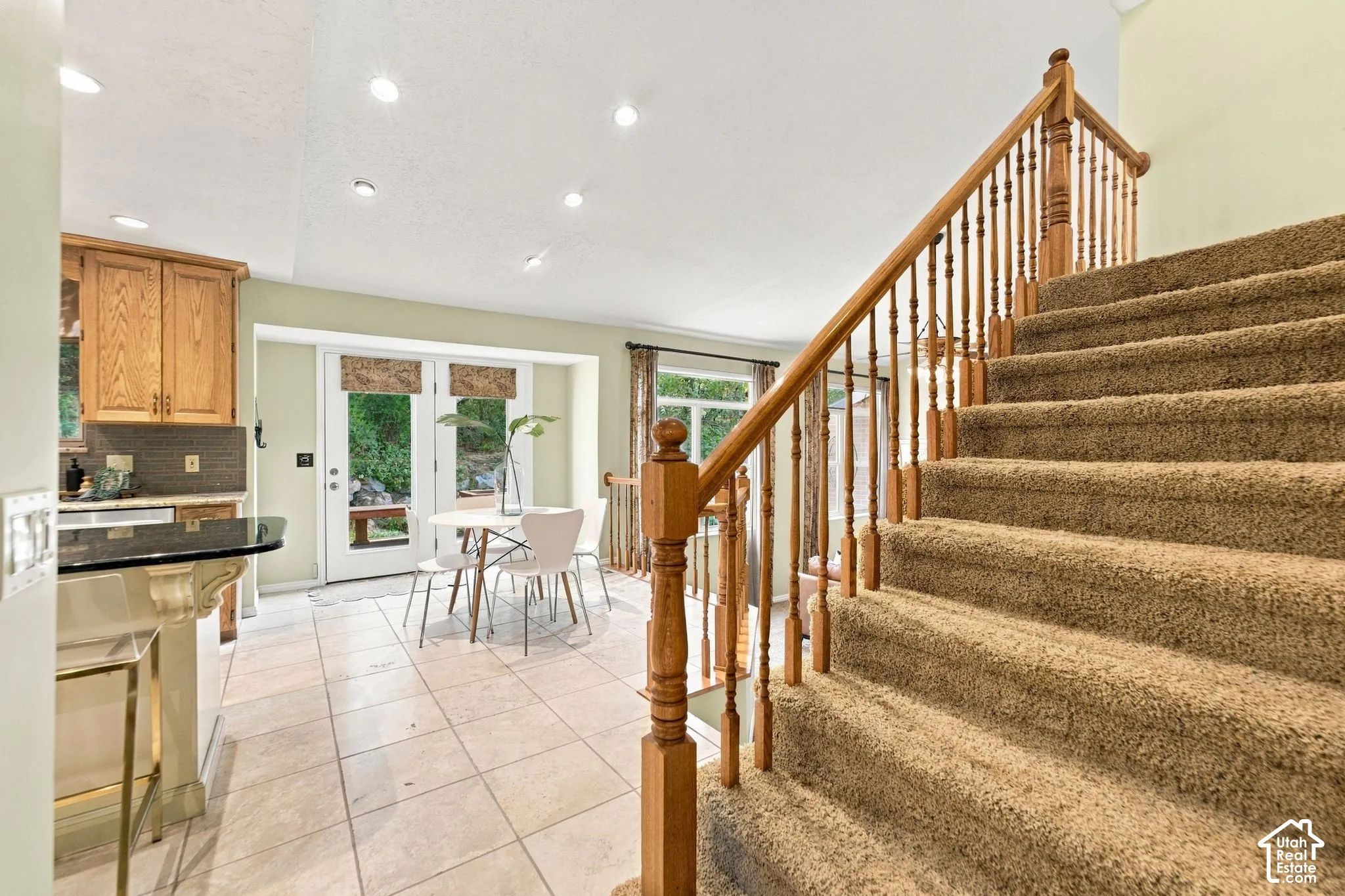 Staircase with wood balusters and handrail, neutral ceramic tile flooring, built-in kitchen cabinetry, and recessed lighting