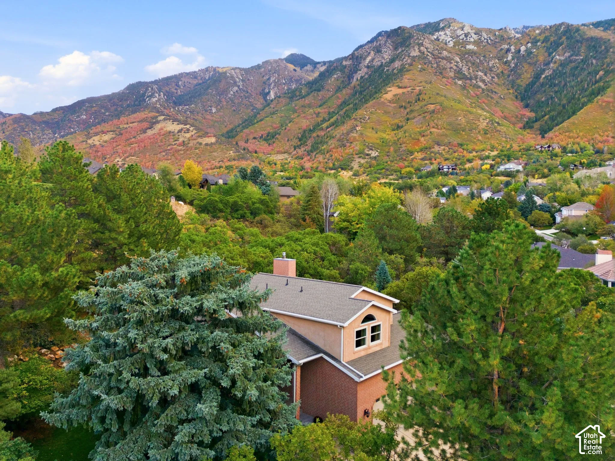 Two-story residence featuring a brick and stucco exterior, chimney stack, arched window, and mountain backdrop