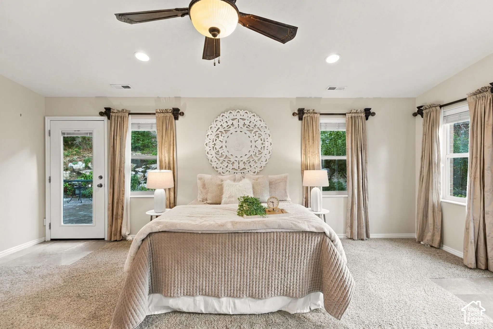 Primary bedroom with vaulted ceilings, neutral wall tones, carpeted flooring, a multi-blade ceiling fan with integrated light fixture, and double glass doors providing outdoor access