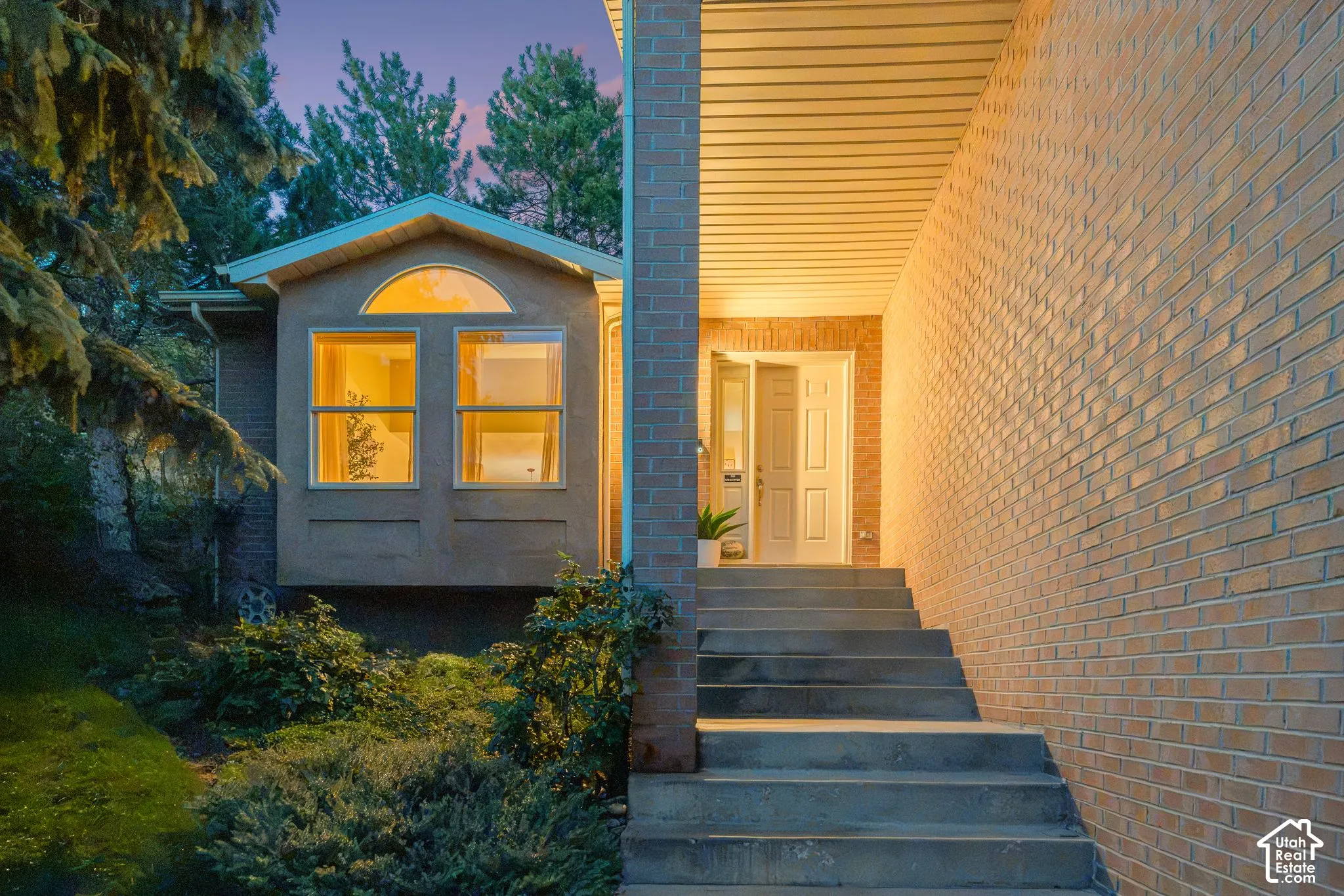 Brick exterior featuring a covered entryway, concrete steps, a paneled front door, and a bay window with a semicircular transom