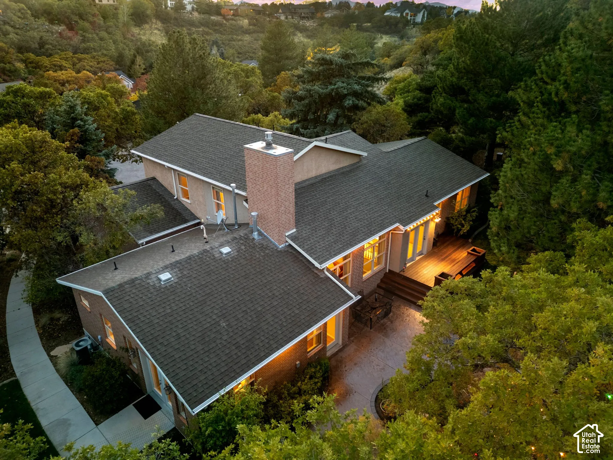Multi-level exterior featuring a brick chimney, wood decking, paved patio, and mature tree canopy