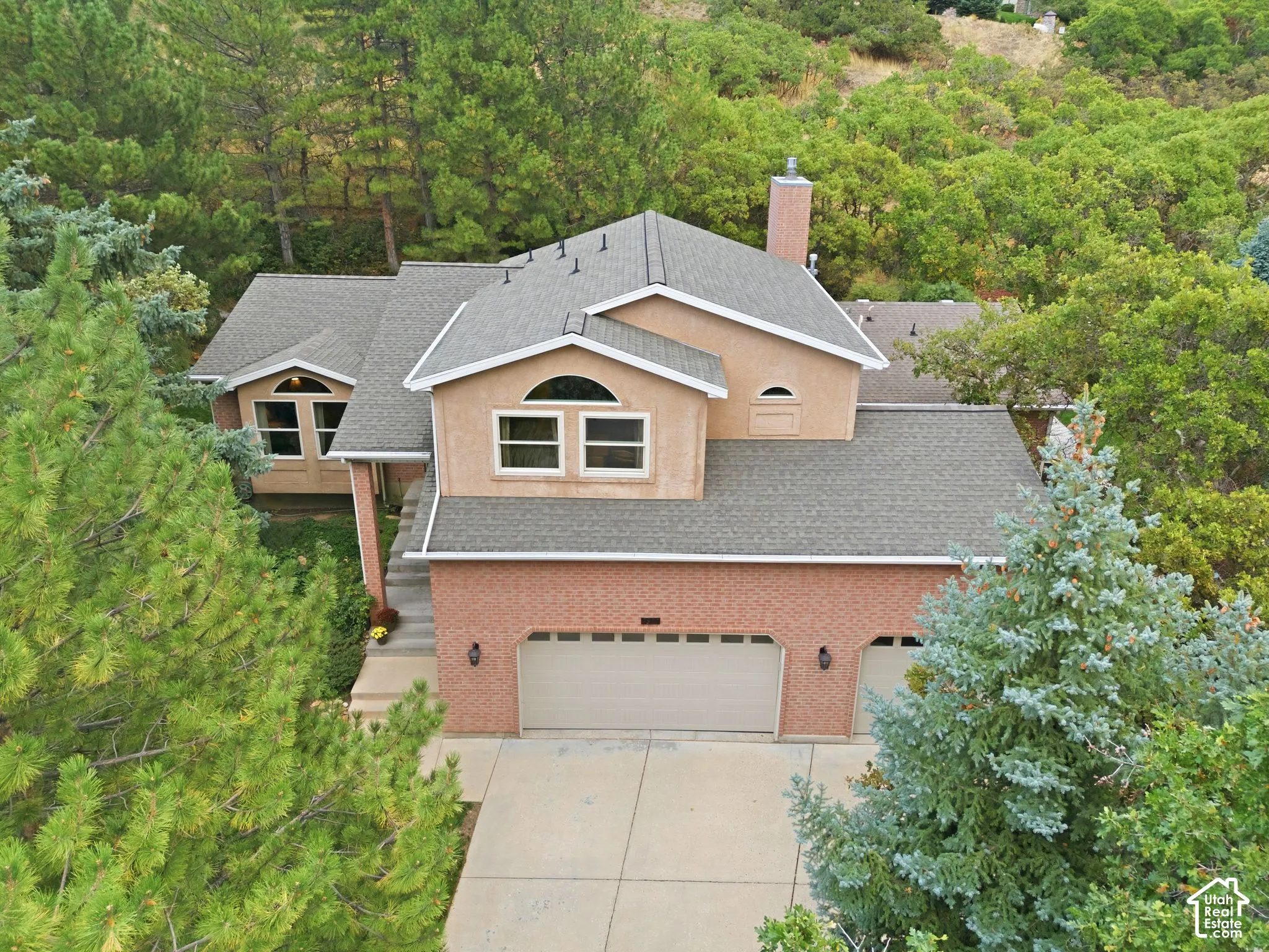 Multi-level residence featuring a brick and stucco exterior, a three-car garage, an asphalt shingle roof, and a chimney