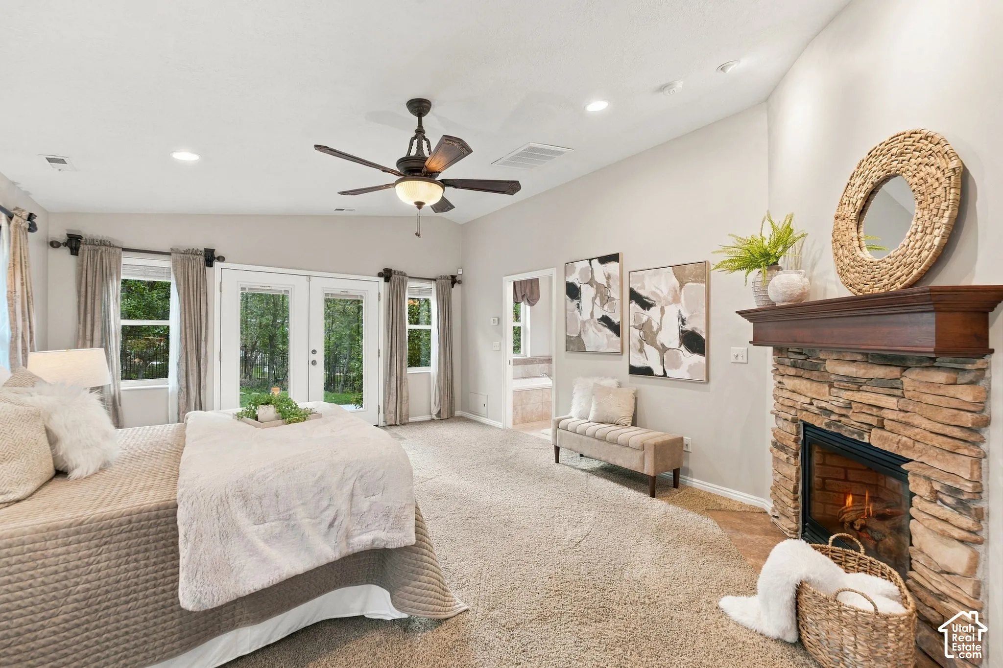 Primary bedroom with vaulted ceilings, neutral wall tones, carpeted flooring, a multi-blade ceiling fan with integrated light fixture, and double glass doors providing outdoor access