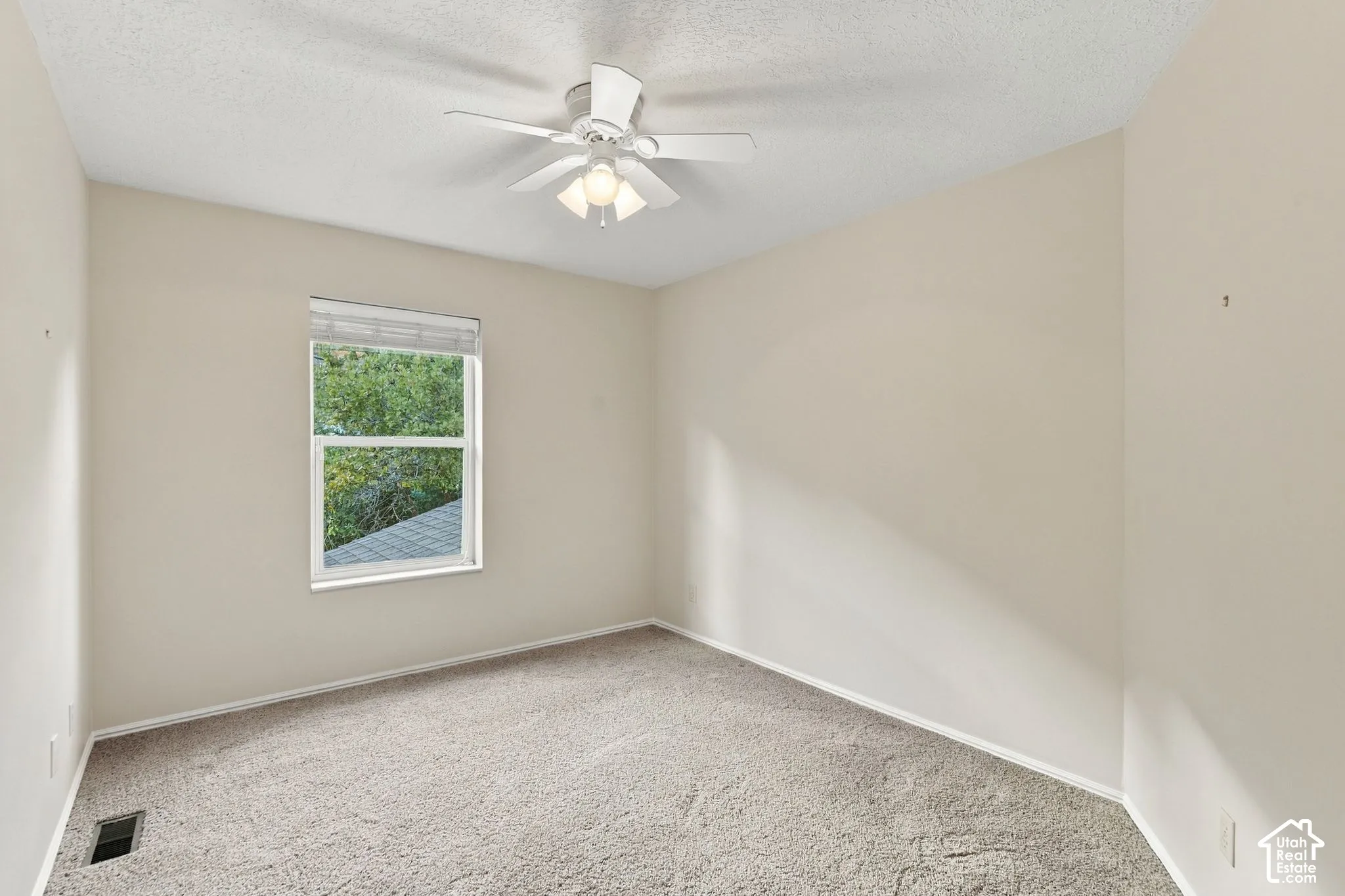 Neutral-toned interior space featuring carpeting, a single-hung window, and a ceiling-mounted fan with light fixture