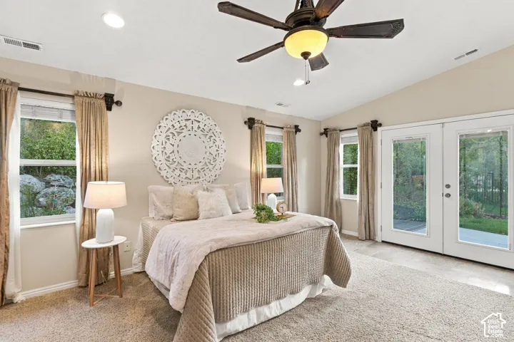 Primary bedroom with vaulted ceilings, neutral wall tones, carpeted flooring, a multi-blade ceiling fan with integrated light fixture, and double glass doors providing outdoor access