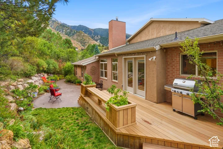 Multi-level wood deck with integrated planter boxes, brick and stucco exterior, paved stone patio, and mountain backdrop