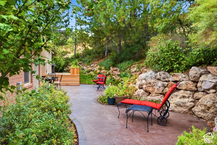 Stamped concrete patio featuring a tiered wood deck, natural stone retaining wall, and mature landscaping