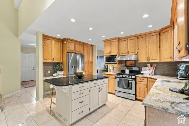 Kitchen featuring light wood cabinetry, a central island with a contrasting stone countertop, built-in stainless steel appliances, and ceramic tile flooring
