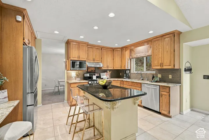 Kitchen featuring custom wood cabinetry, central island with decorative corbels, stone-finish countertops, stainless steel appliances, and recessed lighting
