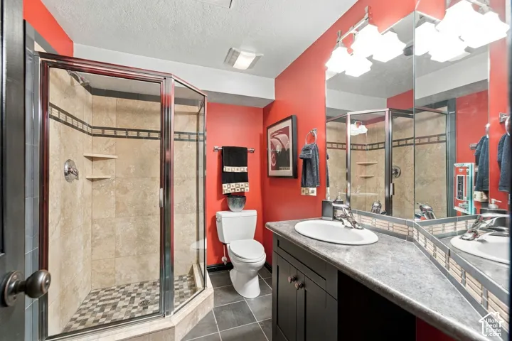 Corner shower with glass enclosure, beige stone-finish tile surround, and mosaic tile floor inlay, paired with a dark-finish vanity featuring a solid-surface countertop, an oval under-mount sink, and a multi-light fixture