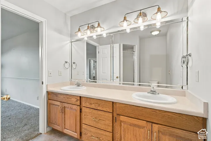 Second Floor Primary Ensuite Bathroom with Dual-sink vanity featuring a light-toned countertop, wood-finish cabinetry, a large wall-mounted mirror, and industrial-style multi-bulb lighting fixtures