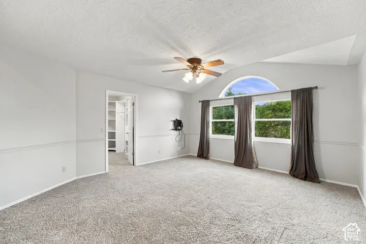 Second Floor Primary Suite with Vaulted ceiling room featuring a central arched window, wall-mounted chair rail molding, neutral carpet flooring, and a ceiling fan with integrated light fixture