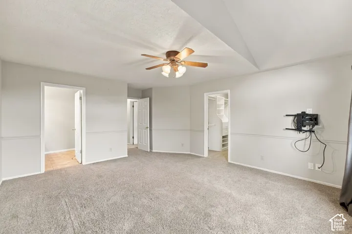 Second Floor Primary Suite with Vaulted ceiling room featuring a central arched window, wall-mounted chair rail molding, neutral carpet flooring, and a ceiling fan with integrated light fixture