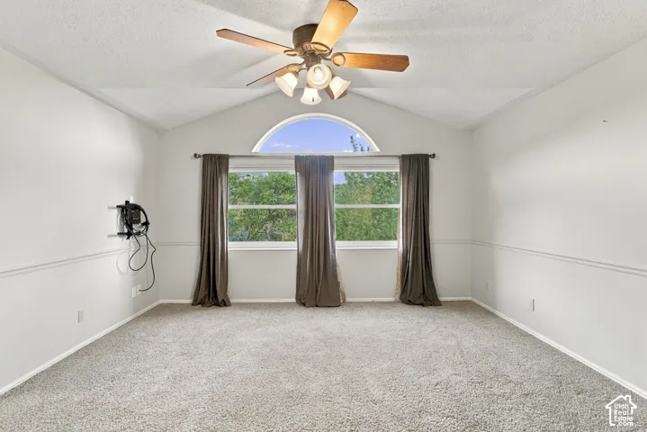Second Floor Primary Suite with Vaulted ceiling room featuring a central arched window, wall-mounted chair rail molding, neutral carpet flooring, and a ceiling fan with integrated light fixture