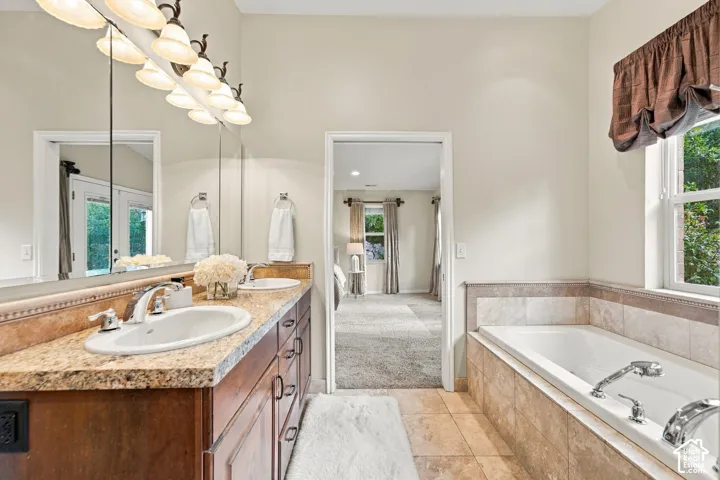Primary Bathroom with Dual-sink vanity with stone-finish countertop, full-width mirror, tile-surround soaking tub, and tile flooring