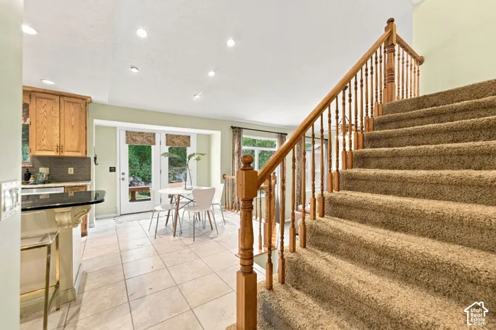 Staircase with wood balusters and handrail, neutral ceramic tile flooring, built-in kitchen cabinetry, and recessed lighting