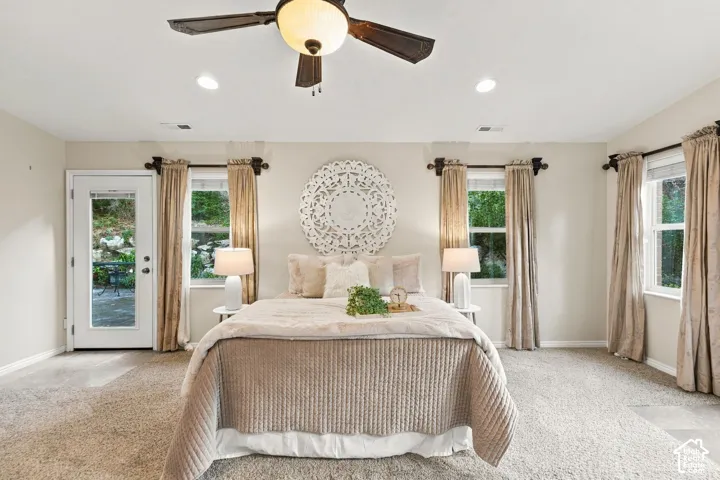 Primary bedroom with vaulted ceilings, neutral wall tones, carpeted flooring, a multi-blade ceiling fan with integrated light fixture, and double glass doors providing outdoor access