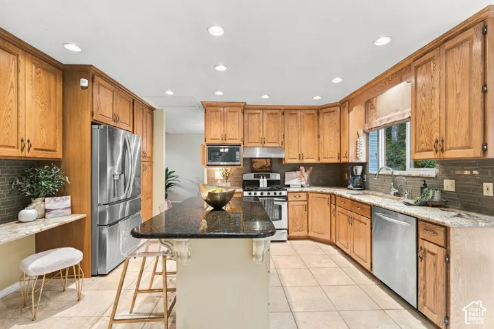 Kitchen featuring custom wood cabinetry, dark stone island countertop, light stone perimeter countertops, recessed lighting, and stainless steel appliances