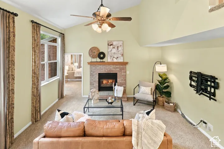 Vaulted ceiling featuring a central lighted ceiling fan, brick fireplace with a wood mantle, and multi-pane window