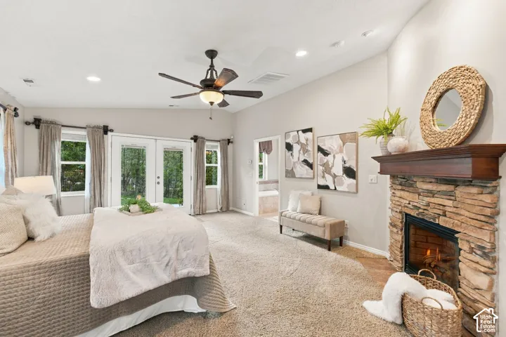 Primary bedroom with vaulted ceilings, neutral wall tones, carpeted flooring, a multi-blade ceiling fan with integrated light fixture, and double glass doors providing outdoor access