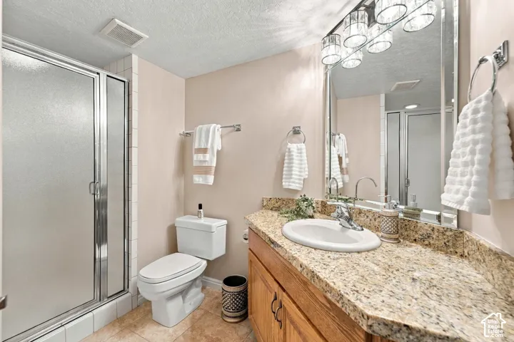 Bathroom featuring a natural stone countertop with an integrated oval basin, wooden vanity cabinetry, polished chrome multi-light fixture, large rectangular mirror, and a walk-in shower with a glass enclosure