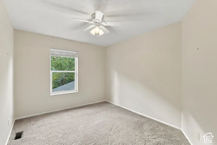 Neutral-toned interior space featuring carpeting, a single-hung window, and a ceiling-mounted fan with light fixture