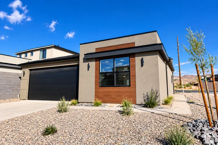 Contemporary exterior featuring smooth stucco finish, horizontal wood-style siding accents, black metal-frame window, and an attached multi-panel garage door