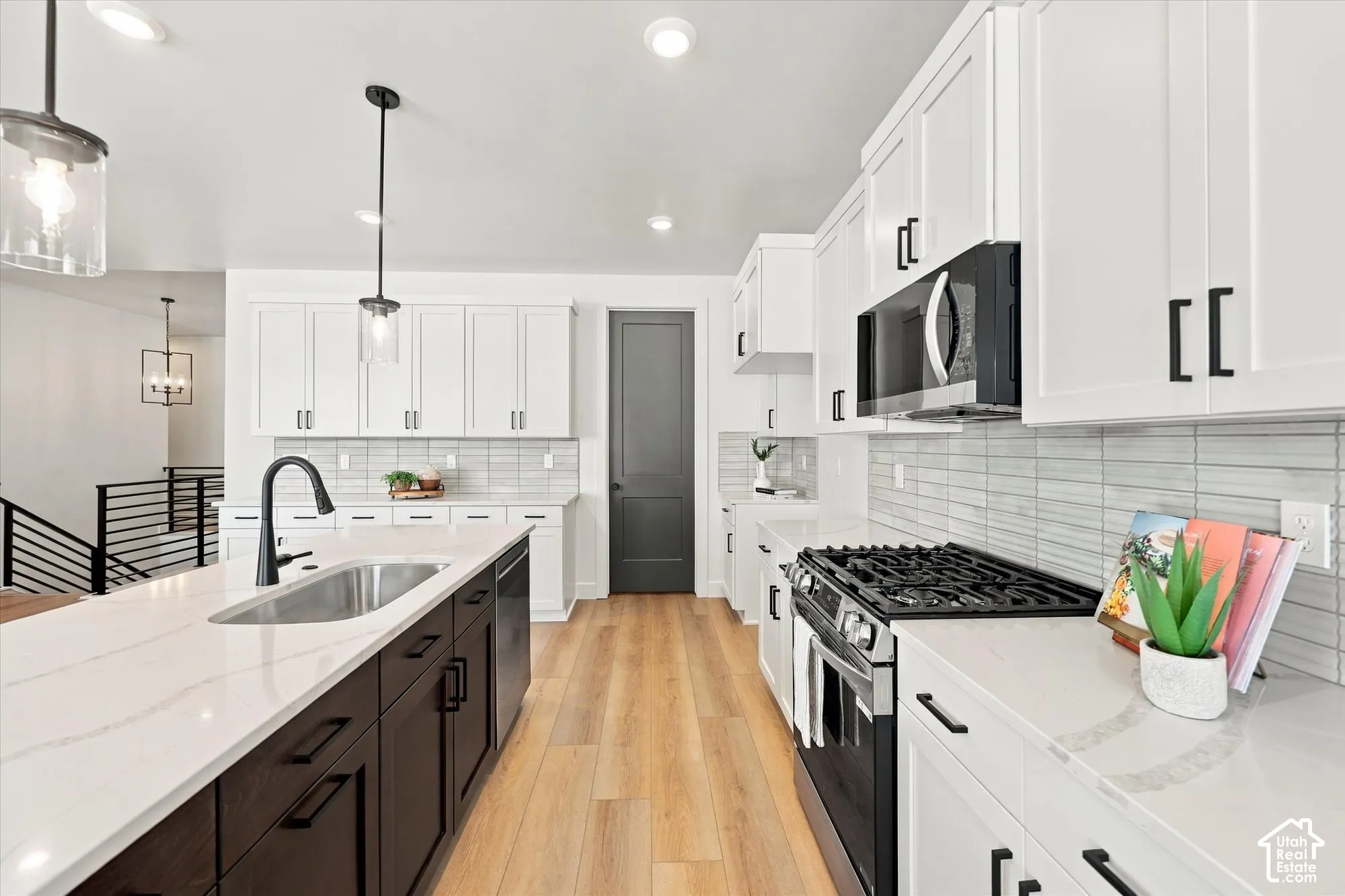 Kitchen featuring white and dark cabinetry, quartz countertops, tile backsplash, wood-finish flooring, and pendant lighting