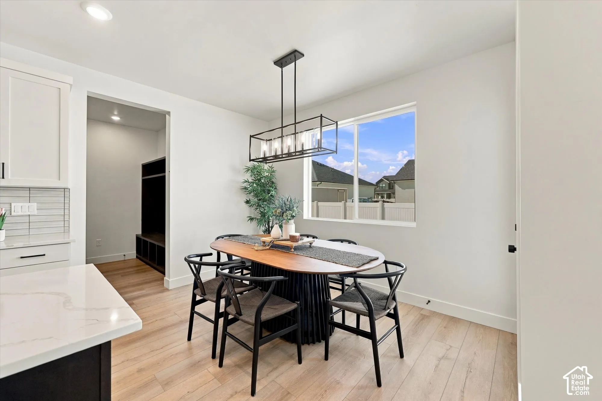 Dining area featuring wood-finish flooring, a geometric linear pendant light, a large picture window, and neutral cabinetry with solid-surface countertops