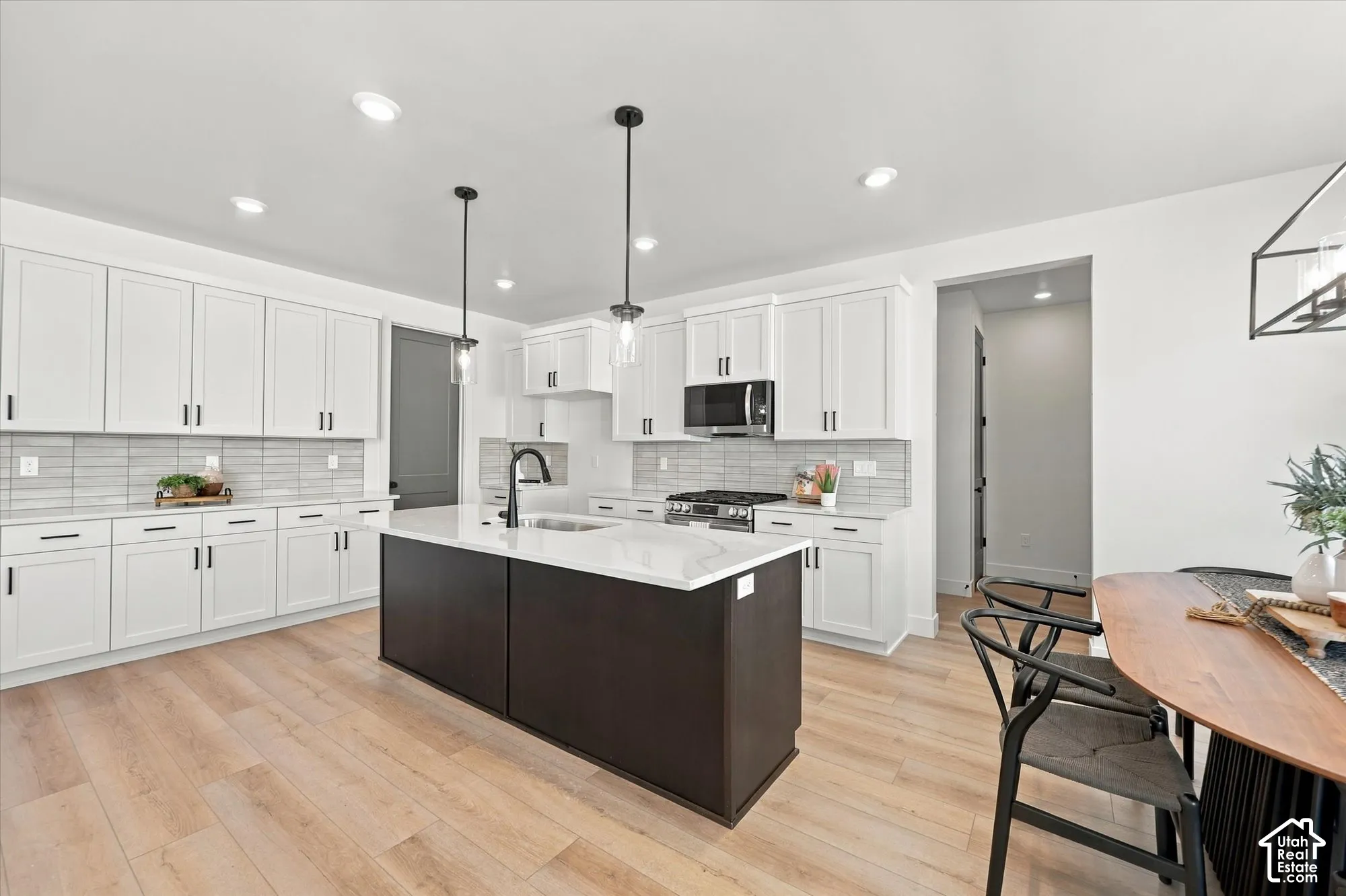 Kitchen featuring white cabinetry, a contrasting dark-toned center island with a stone-finish countertop, stainless steel appliances, linear tile backsplash, and wood-finish flooring