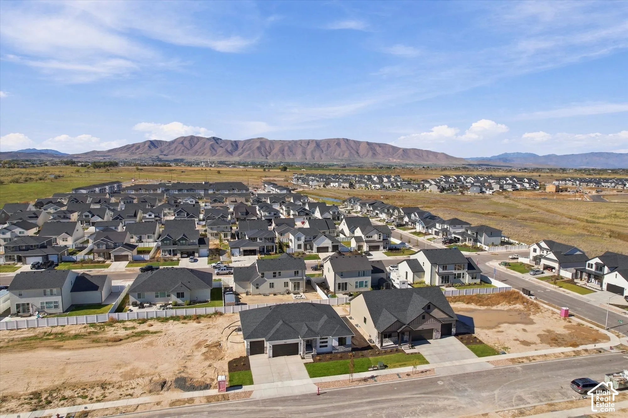 Aerial perspective of a residential neighborhood featuring multi-gabled rooflines, concrete driveways, paved street infrastructure, and a prominent mountain range backdrop
