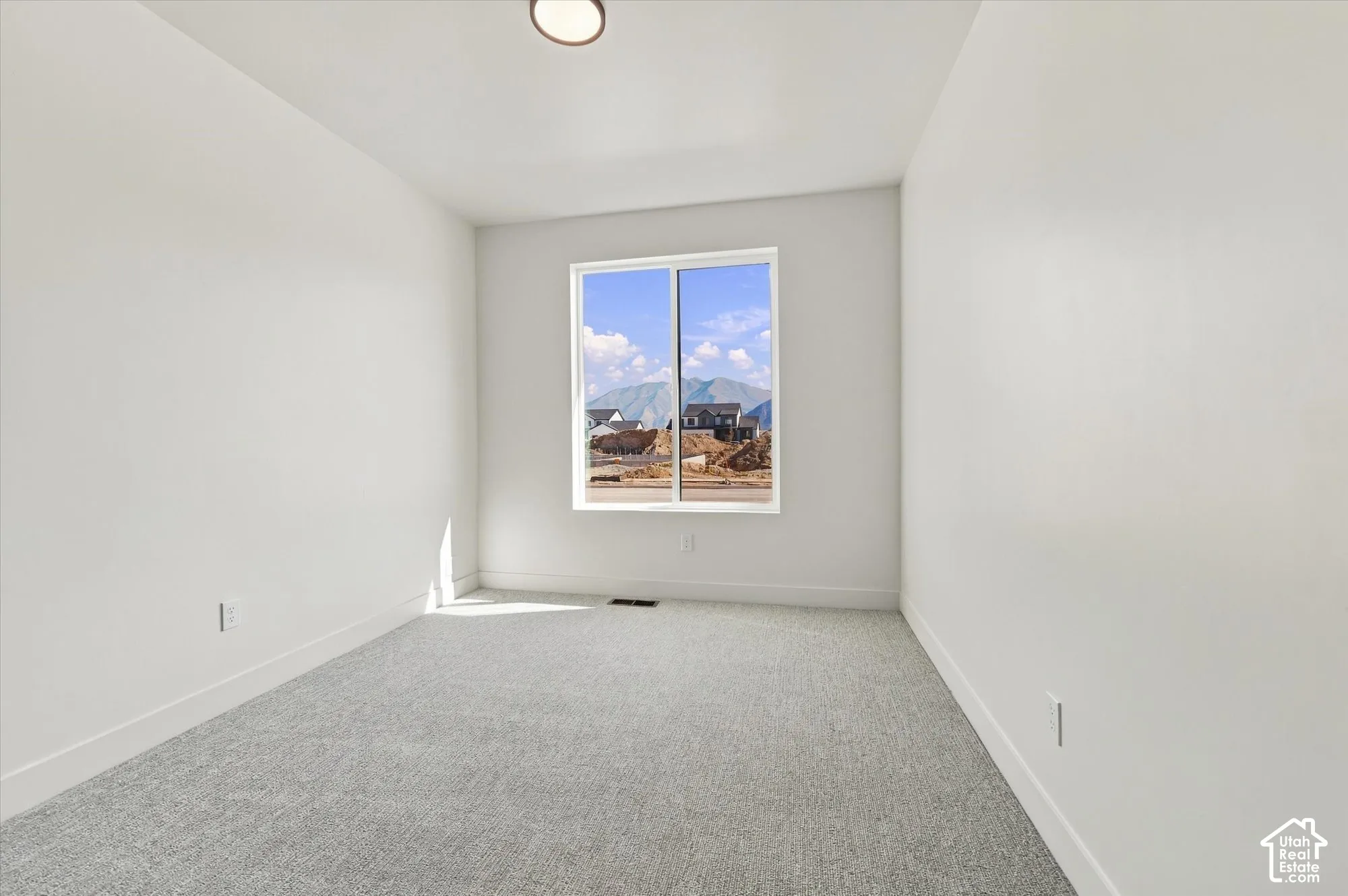 Neutral-toned carpeted flooring, white walls, flush-mount ceiling lighting, and a single-pane sliding window showcasing a mountain backdrop